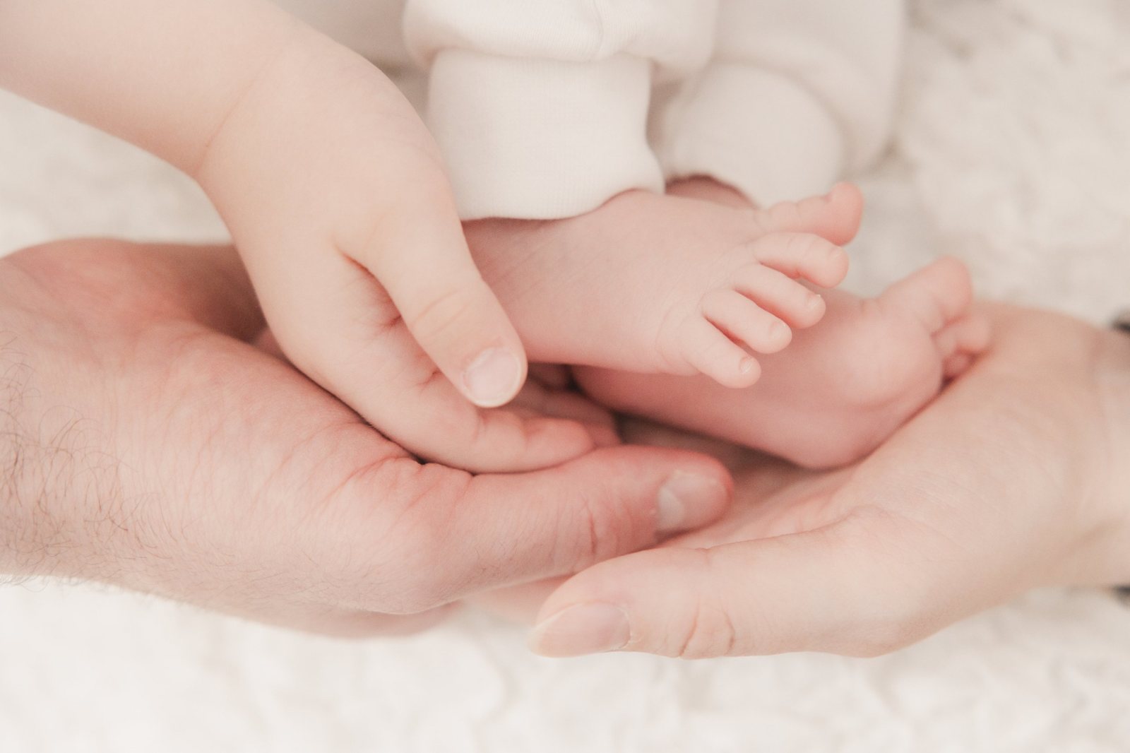 Babyfüße in den Händen von Papa und großem Geschwisterchen