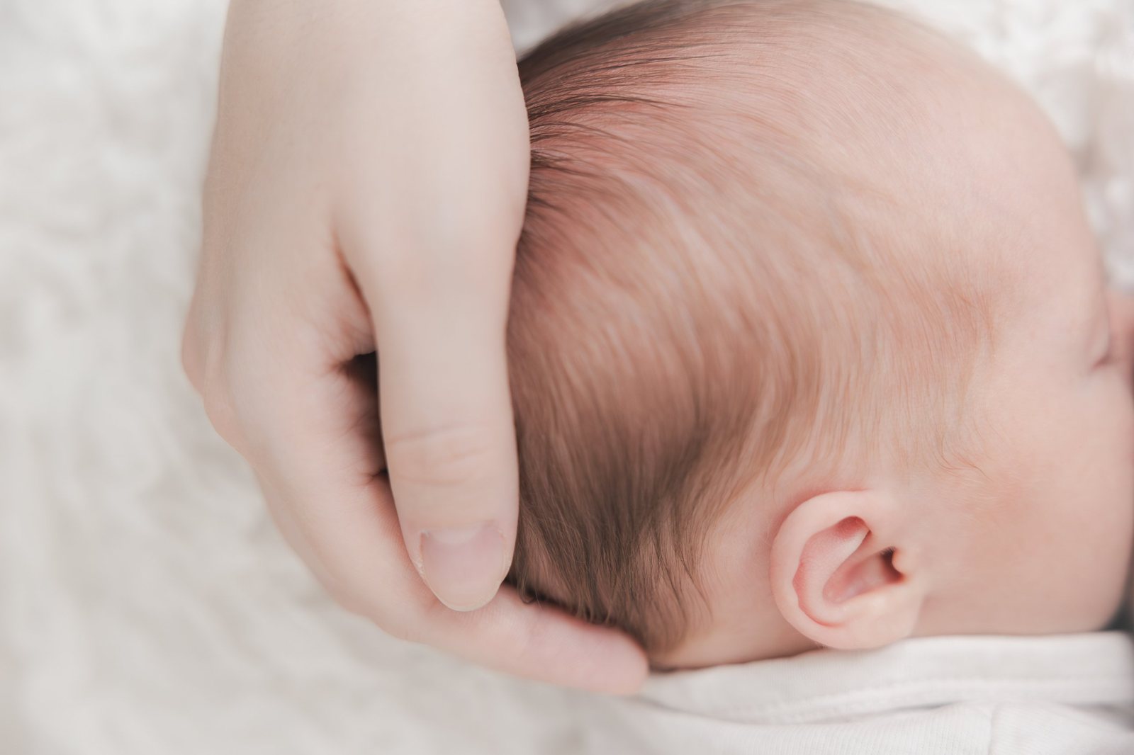 Mamas Hand hält zärtlich das Köpfchen ihres Neugeborenen