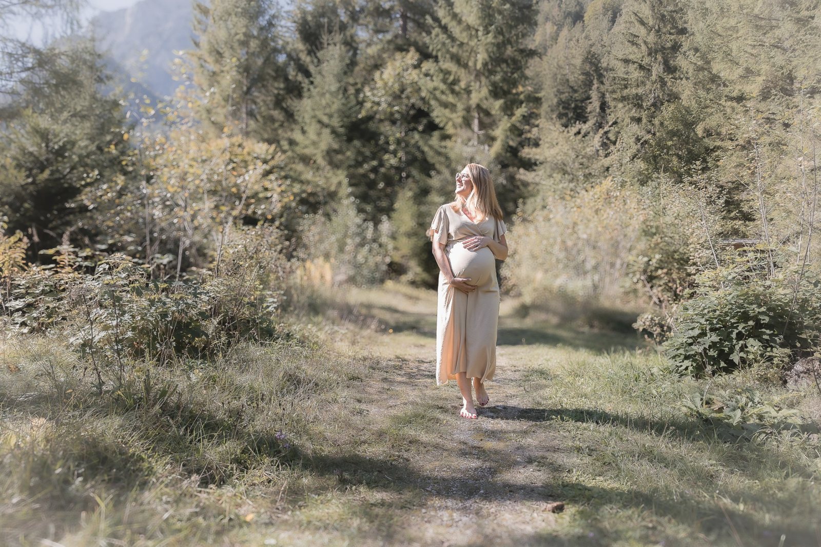 Schwangere Frau geht barfuß einen sonnigen Waldweg entlang