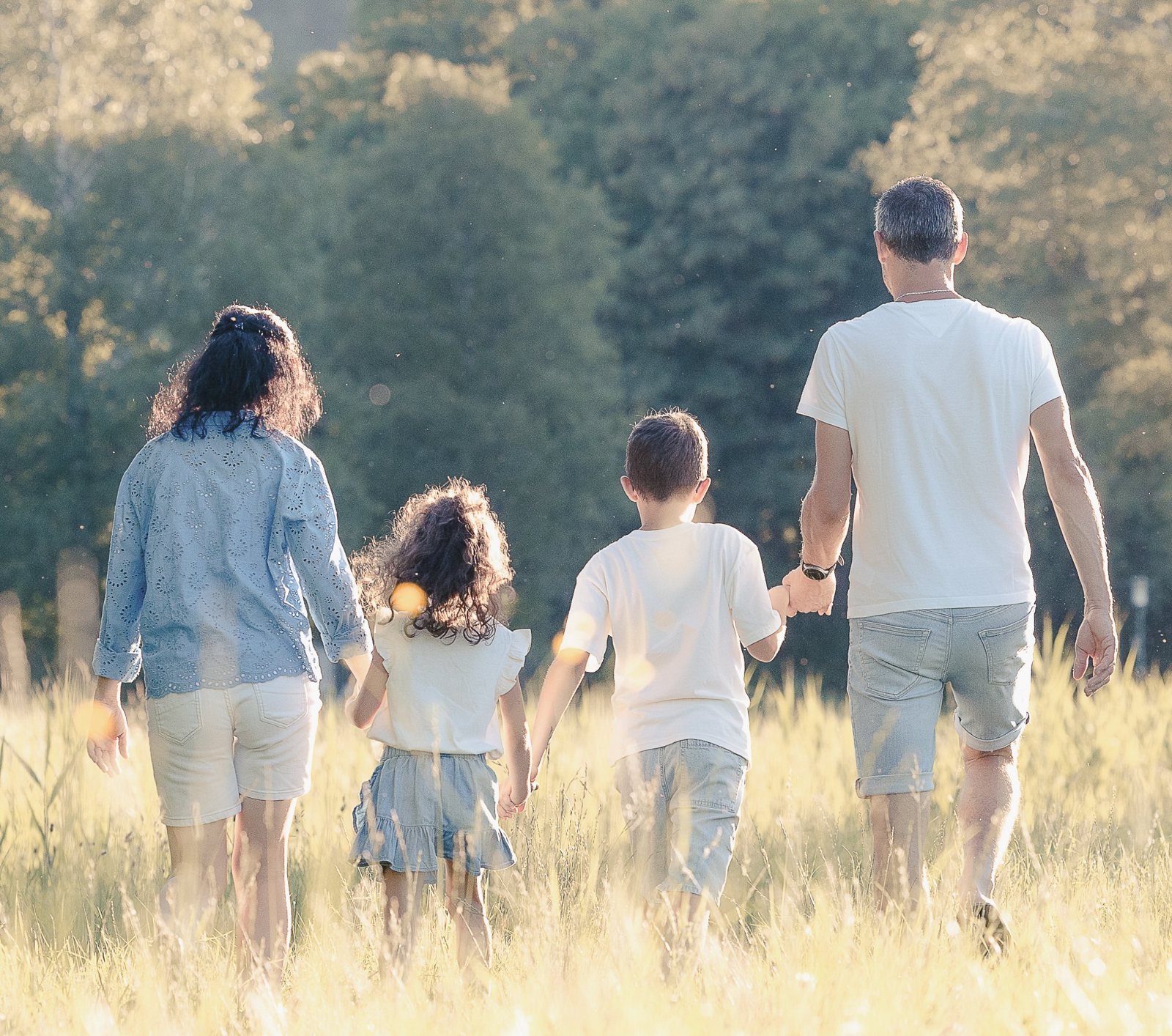 Familie geht Hand in Hand durch eine sonnige Wiese