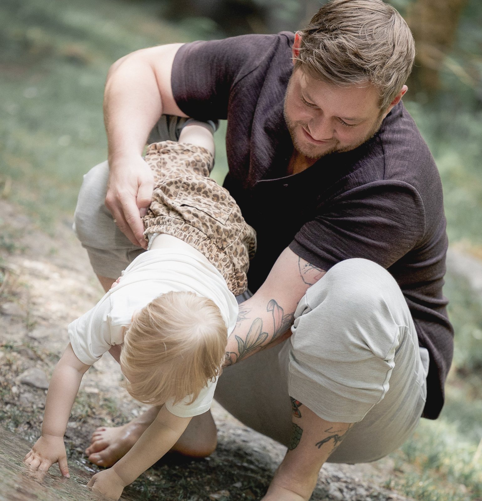 Papa hält sein Kleinkind, das mit den Händen ins Wasser greift