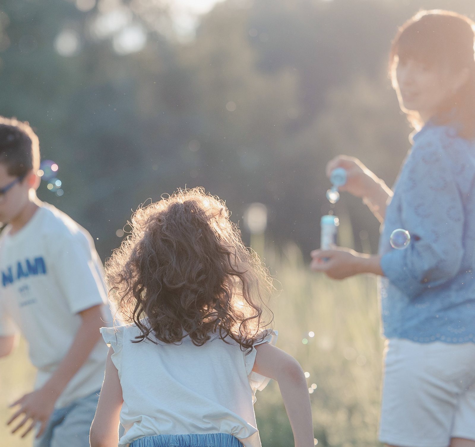 Mädchen mit Locken läuft in der Abendsonne zu ihrer Mama, die Seifenblasen macht